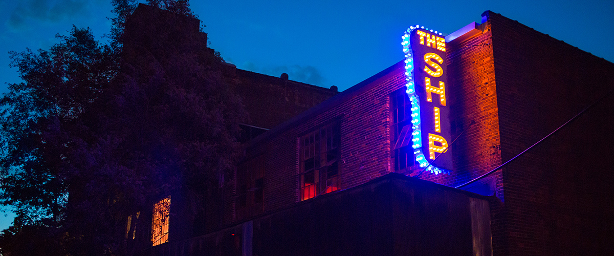 Neon sign in blue and yellow reading "The Ship"